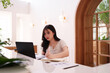 © snowing12 - Young Asian woman remote worker using laptop computer focused professional writing notes cafe bright modern contemporary workspace for productivity