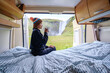 © Fokke Baarssen - A traveler sits inside a cozy camper van, sipping coffee while admiring stunning Icelandic waterfalls. The lush green landscape and cascading water create a peaceful morning atmosphere.