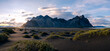 © Fokke Baarssen - The Vestrahorn mountains rise against a dramatic sky, while green grass peeks through black sand dunes, highlighting Icelands breathtaking beauty at sunset.