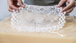 © HI Pictures - In an art studio with an environment adorned with artistic paintings in the background, a beautiful middle-aged woman artist is working on a lace pattern design on a clay plate at a table