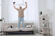 © SHOTPRIME STUDIO - Energetic man celebrating success while standing on a sofa in a bright, modern living room. His excited expression showcases the joy of achievement and inspiration.