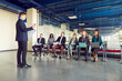 © Studio Romantic - Man speaker talking on a work meeting in modern office in front of a small group of confident diverse company employees sitting on chairs in a row with laptops on a business conference.