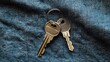 © Suphawan - Top view of house keys and car key on a round keyring, placed on textured denim fabric background, representing everyday lifestyle