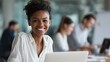 © Johannes - smiling young african american businesswoman working on a laptop at her desk in a bright modern office with colleagues in the background no logos no brands ar 169