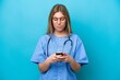 © luismolinero - Young surgeon doctor woman isolated on blue background sending a message with the mobile