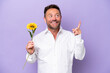 © luismolinero - Middle age caucasian man holding sun flower isolated on purple background pointing up a great idea