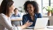© NafiliaEmil - Close up happy young african american businesswoman using laptop with laughing female mentor in coworking boardroom at meeting. Smiling diverse woman managers. Detailed high quality image.