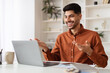 © Prostock-studio - Video Conference. Portrait of excited Middle Eastern business manager having web call using laptop sitting at desk at workplace in home office, talking and gesturing at webcam, free copy space banner