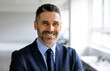 © Prostock-studio - Portrait of happy confident middle aged businessman in suit looking and smiling at camera, posing in office interior, free space. Ceo manager and boss, successful work, career concept