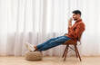 © Prostock-studio - Rest Concept. Happy Arab guy drinking coffee sitting on chair in living room. Casual man relaxing, enjoying weekend free time or break from work, free copy space, profile side view, full body length