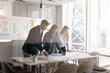 © fizkes - Positive young multiethnic coworkers meeting in collaboration room for teamwork, discussing paper sales marketing reports, planning startup strategy. Through glass wall view
