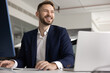 © fizkes - Positive handsome young Caucasian professional man working at laptop, using large monitor, looking away, smiling, laughing. Happy successful legal expert, CEO, executive candid portrait
