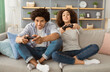 © Prostock-studio - Emotions from online games during self-isolation of covid-19 and entertainment at home. Excited young african american male and female playing with joysticks sitting on sofa in living room interior