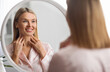 © Prostock-studio - Beautiful Mature Woman Looking At Mirror And Touching Her Soft Skin On Neck, Attractive Middle Aged Female Smiling To Reflection, Enjoying Anti-Aging Skincare Routine At Home, Selective Focus