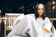 © Anastasia Visuals - A young woman of mixed ethnicity relaxes in a modern outdoor lounge, exuding calm confidence in a stylish outfit.
