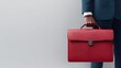 © NingPhattraphorn - A businessman holding a sleek red briefcase, dressed in formal attire, against a minimalist background, conveying professionalism and style, Business banner with a blank space for text
