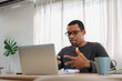 © eggeeggjiew - Focused African man communicates in a virtual meeting, using his laptop in a home office.