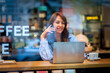 © sepy - Confident woman witting in a cafe and using smartphone and laptop