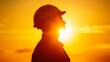 © Yevhen - Silhouette of construction worker in hard hat against bright orange sunset symbolizing dedication