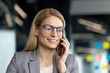 © Liubomir - Businesswoman in glasses smiling while talking on a phone in an office