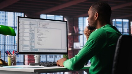 Black IT expert looking at user interface on computer at home office, typing and programming code on terminal window. Coding application used by technician writing script in loft. Camera B.