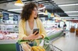 © Serhii - Customer using smartphone while shopping groceries in supermarket