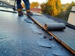 © Olya - Worker installing rolled roofing material on a flat rooftop during autumn with trees in background under clear weather