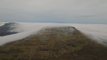 Wall Mural - aerial drone shot of a mountain in the scottish highlands, with clouds dramatically spilling over th