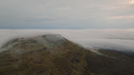 Wall Mural - aerial drone shot of a mountain in the scottish highlands, with clouds dramatically spilling over th