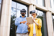© sofiko14 - A diverse couple explores augmented reality using VR headsets and a tablet outdoors near a building.