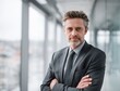 © CaptureCollabStudios - A confident man in a suit with crossed arms poses in a contemporary office. Natural light flows through large windows, creating a bright atmosphere. The space features a sleek design.