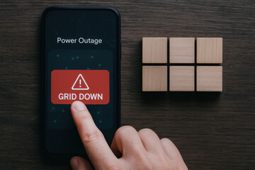 Power outage alert on smartphone screen with finger pressing grid down button indicating electrical power failure risk