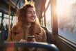 © Atchariya63 - Young woman curly hair brown coat sitting bus holding smartphone sunlight smiling morning city