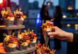 © Soeb Kaes - Photo of a hand holds a gourmet appetizer cone filled with cheese, fruit, and cured meats at an evening event with city lights in the background