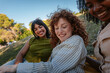 © bernardbodo - Three young women enjoying a picnic, laughing and relaxing in a park