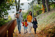 © Halfpoint - Sisters and parents walking in park during warm autumn day.