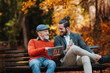 © Halfpoint - Senior father and his son sitting on bench by lake in nature, looking at tablet.