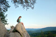 © bilanol - Woman hiker seated alone on rocky mountain cliff enjoying view of nature on wilderness trail. Active way of life concept