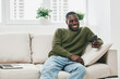 © SHOTPRIME STUDIO - Happy man using smartphone at home, wearing a cozy olive green sweater, comfortable in a bright modern living space, highlighting casual lifestyle and relaxation