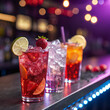 © MdAriful - Close up of three colorful cocktails garnished with fruit on a bar with blurred background lights