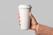 © andrew - A hand holds a white reusable coffee cup against a gray background