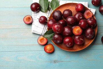 Wall Mural - ripe cherry plums, cloth and green leaves on light blue wooden table, flat lay. space for text