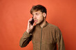 © mathiasalvez - Young Caucasian man talking on smartphone in brown jacket on orange background