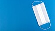© isrofil - A single, white, disposable face mask rests on a vibrant blue surface.