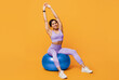 © Prostock-studio - Happy african american woman sitting on fitball, ready for training, raising hands up, stretching and smiling to camera over yellow studio background. Active lifestyle concept