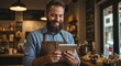 © Cintia - Happy barista checks orders on tablet in his shop. He wears an apron and a light blue striped shirt while working in his food service business.