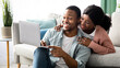 © Prostock-studio - Happy young black couple shopping online at home, using laptop, copy space. Emotional african american guy showing his girlfriend something exciting on Internet, holding notebook