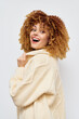 © SHOTPRIME STUDIO - Happy young woman with curly hair wearing a cozy cream sweater, smiling joyfully against a plain white background Her engaging expression exudes warmth and confidence