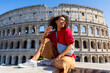 © Bogdan Pictures - A cheerful and vibrant young woman strikes a pose in front of the iconic Colosseum in Rome, proudly showcasing the stunning beauty and grandeur of this ancient landmark that attracts many tourists