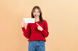 © sitthiphong - Happy Asian business woman standing and hold blank paper or gift voucher mockup on beige color background.